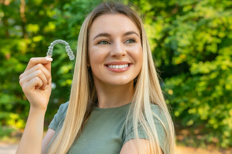 girl holding clear aligner, blonde hair smiling girl, cosmetic dentistry