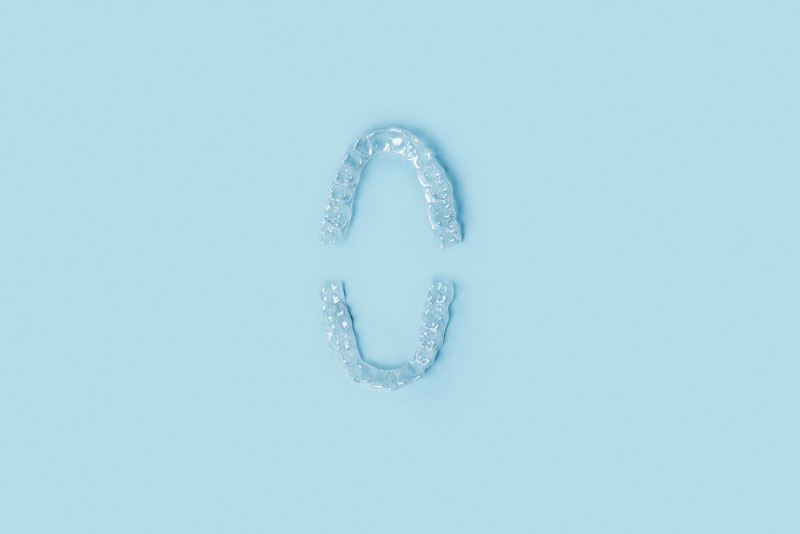 Top and bottom clear dental aligners placed on a light blue background, used for orthodontic teeth straightening treatment.